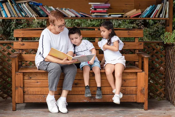 Читання книжки. Бабуся читає дітям в саду на лавці . — стокове фото