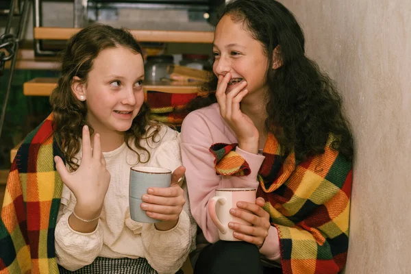 Feliz chicas jóvenes amigos hablando y riendo sentado envuelto en una manta en casa. — Foto de Stock