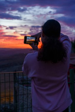 Arkaya bakan genç kadın inanılmaz günbatımının fotoğrafını çekiyor..