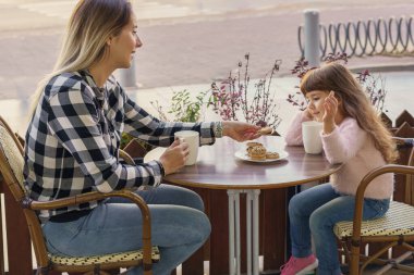 Neşeli bir anne ve küçük kız açık hava restoranında öğle yemeğinin tadını çıkarıyorlar. Aile birlikte vakit geçiriyorlar..