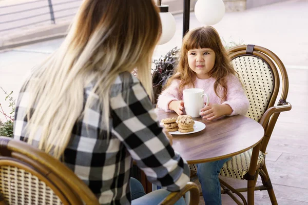 A happy mother and daughter eat cookies, and drink tea while spending the day at the cafe together. — Stock Photo, Image