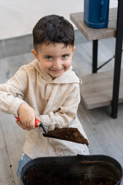 Healthy organic food concept. Child shovels ground, putting soil in flower pot. — Stock Photo, Image