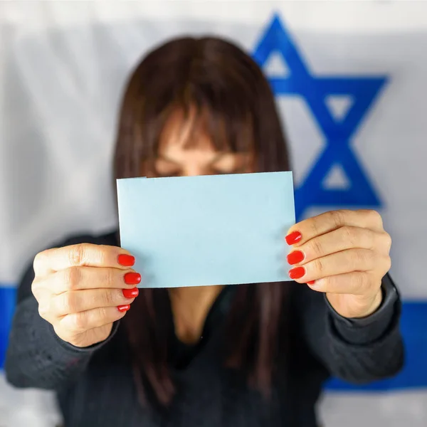 Nő, aki névjegykártyát vagy üres szavazólapot tart, Blue Paper Front Of Face az izraeli lobogó hátteréről. A szöveg helye, mockup — Stock Fotó