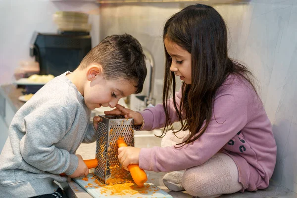 Cute children shredding carrot in kitchen. — Stock Photo, Image