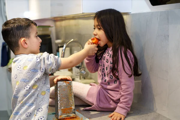 Cute children shredding and eating carrots in kitchen. — Stock Photo, Image