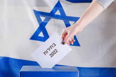 Israeli woman votes on election day. Close up of hand. Hebrew text Elections 2022 on Israel flag background. Israel heads for new election as fragile coalition collapses. clipart