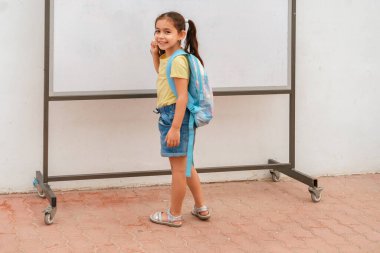 Happy Child With Backpack Writing On A Whiteboard In School.
