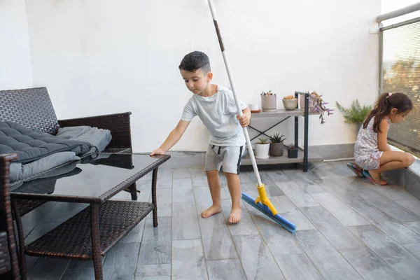 Funny young child cleaning floor at home. Boy washing floor with mopping stick in balcony of modern apartment. Male household helping tidy house. Children happy helping with home cleaning chores.