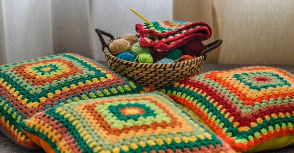 Granny square crochet. Home made creations. Colorful wool yarns in a straw basket on a couch. Handmade knitting, knit pillows, and a cute atmosphere.