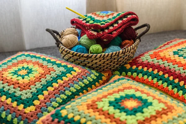 Granny square crochet. Home made creations. Colorful wool yarns in a straw basket on a couch. Handmade knitting, knit pillows, and a cute atmosphere.
