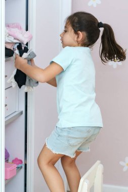 Uzun siyah saçlı güzel bir kız gardırop siparişini getiriyor, her şeyi dolaba koyuyor. İçinde çocuk kıyafetleri olan gardırop..