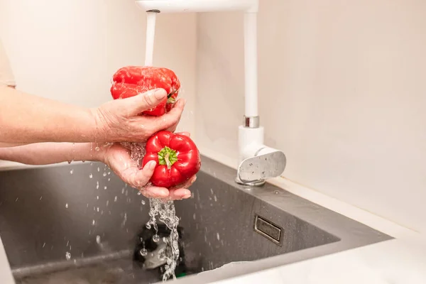 Woman washing vegetables. Close-up of woman hands washing red bell pepper.