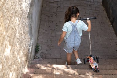 Merdivenlerden inerken küçük bir kızın scooter 'ını taşıması..