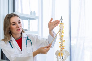Omurga modelini gösteren steteskopla tedavi edici kadın doktorunun yakın çekimi hastane geçmişinde olumlu duygular barındırıyor..