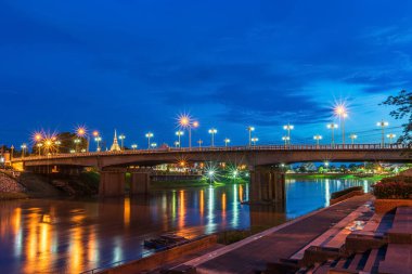 Phitsanulok City, Tayland 'da gece vakti köprüde (Naresuan Köprüsü) yürüyüş, bisiklet ve egzersiz yapmak ve Nan Nehri üzerinde yürüyüş yapmak için parktaki yolda güzel ışıklar görülüyor.. 
