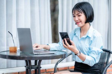 Diş telleriyle gülümseyen Asyalı serbest çalışan iş kadını akıllı telefondan mesaj yazıyor. Laptop bilgisayarıyla kafede kahve fincanı ile çalışıyor. Business Lifestyle.