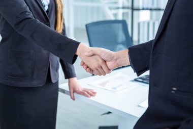 İş kadını ve işadamı, sözleşme imzalandıktan sonra ofis arka planında el sıkışırken, iş dünyası güven verici ve başarılı bir konsept olduğunu ifade etti.