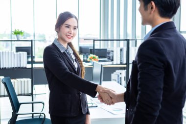 İş kadını ve işadamı, sözleşme imzalandıktan sonra ofis arka planında el sıkışırken, iş dünyası güven verici ve başarılı bir konsept olduğunu ifade etti.