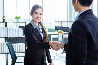 İş kadını ve işadamı, sözleşme imzalandıktan sonra ofis arka planında el sıkışırken, iş dünyası güven verici ve başarılı bir konsept olduğunu ifade etti.