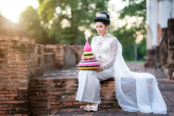 タイの白い伝統衣装を着た美しいアジアの女性がクラトンを保持し 古代都市でパゴダ寺院の前に座っているタイ クラトン祭り トランスジェンダーモデル — ストック写真