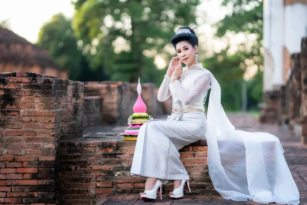 タイの白い伝統衣装を着た美しいアジアの女性がクラトンを保持し 古代都市でパゴダ寺院の前に座っているタイ クラトン祭り トランスジェンダーモデル — ストック写真