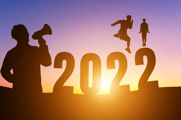 Mutlu yıllar 2022, Siluet. Megafonla bağıran yakışıklı bir adam ve zıplayan bir adam ufuk çizgisinde mutlu bir sabah geçiriyor. Sağlık ve Mutlu Yıllar konsepti..
