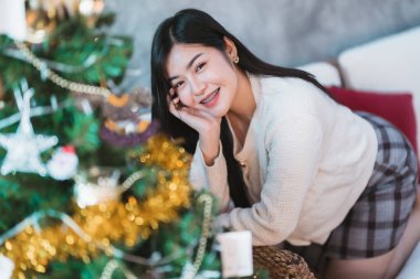 Güzel, güzel, pozitif bir gülümseme. Genç Asyalı kadın, Noel ve yeni yıl tatilleri boyunca evdeki Noel ağacını süslüyor..