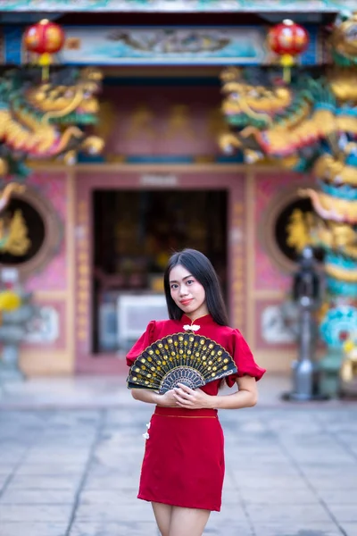 肖像画美しい笑顔アジアの若い女性は タイの中国の神社で中国の旧正月の祭りのための中国のファニングを開催し 赤い伝統的な中国のChongsam装飾を身に着けている — ストック写真