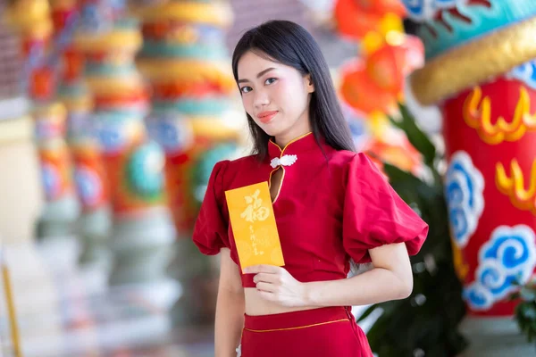 肖像アジアの若い女性はそれに書かれた中国語のテキストの祝福と黄色のアンパオ封筒を保持赤い伝統的な中国のChengsam装飾を身に着けている幸せな中国の新年のための幸運 — ストック写真
