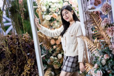 Gülümse mutluluk portresi. Güzel Asyalı kadın. Evde, kafede ve gül arkaplanda kalın giysiler giyiyor.