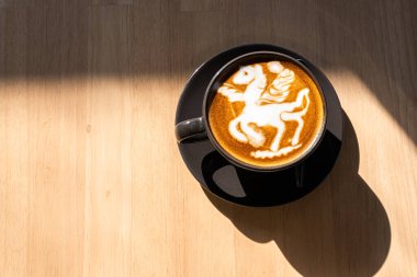 Hot coffee latte with latte art in the form of a horse milk foam in cup mug on wood desk on top view. As breakfast In a coffee shop at the cafe,during business work concept