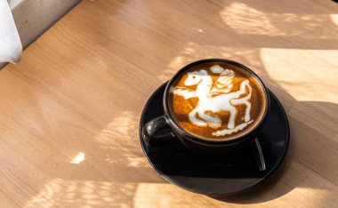 Hot coffee latte with latte art in the form of a horse milk foam in cup mug on wood desk on top view. As breakfast In a coffee shop at the cafe,during business work concept