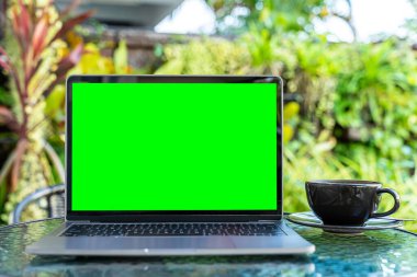 Mockup of laptop computer with empty screen with coffee cup and smartphone on table of the coffee shop outdoor background,Green screen