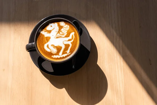 Hot coffee latte with latte art in the form of a horse milk foam in cup mug on wood desk on top view. As breakfast In a coffee shop at the cafe,during business work concept