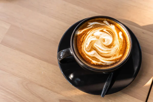 Hot coffee latte with latte art in the form of milk foam in cup mug on wood desk on top view. As breakfast In a coffee shop at the cafe,during business work concept