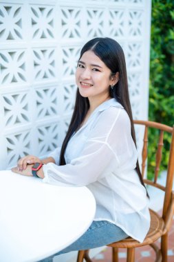 Güzel mutlu Asyalı kadın gezginin modern portresi şık giyinen, güzel beyaz elbiseler giyen ve kot pantolon giyen kahve dükkanının arka planında eğlenen.