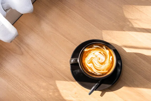 Hot coffee latte with latte art in the form of milk foam in cup mug on wood desk on top view. As breakfast In a coffee shop at the cafe,during business work concept