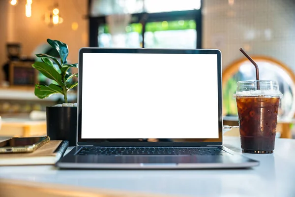 Mockup of laptop computer with empty screen with notebook,ice coffee and smartphone on table side the window in the coffee shop at the cafe,White screen