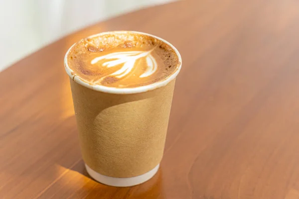 Hot coffee latte with latte art milk foam in cup made of paper on wood desk on top view. As breakfast In a coffee shop at the cafe,during business work concept