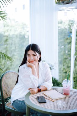 Güzel mutlu Asyalı kadın gezginin modern portresi şık giyinen, güzel beyaz elbiseler giyen ve kot pantolon giyen kahve dükkanının arka planında eğlenen.