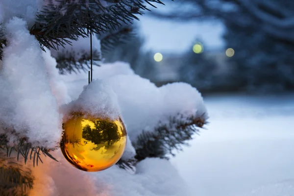 Bright Gold Ornament Hangs From Snow Covered Christmas Tree — Stock Photo, Image