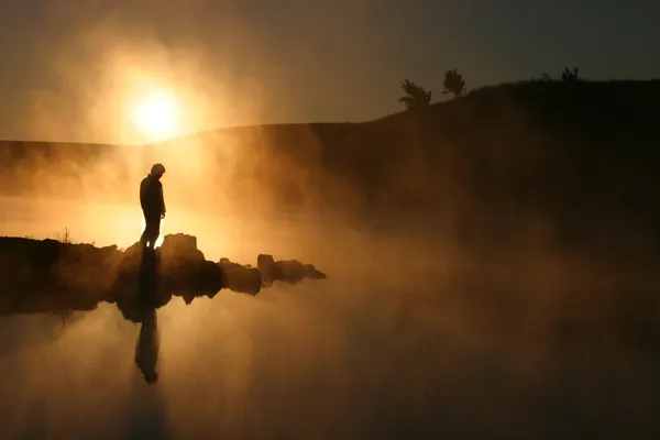 El sol de la mañana y la niebla rodean al caminante con siluetas en un lago tranquilo — Foto de Stock