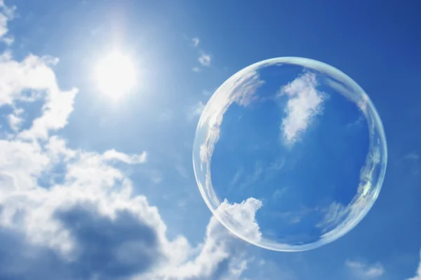 Floating Soap Bubble Against Clear Sunlit Blue Sky and Clouds