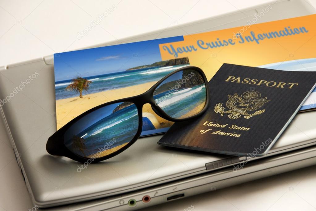 Sunglasses reflect an exotic Caribbean beachwith international passport, cruise information and travel laptop