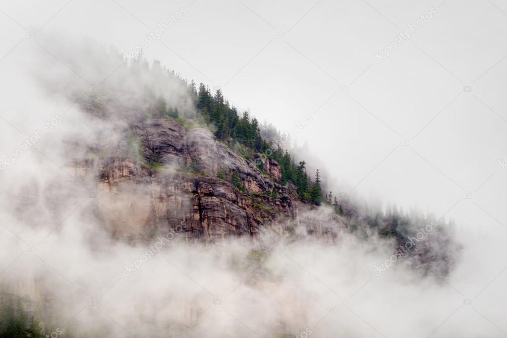 Mountain bluff face is shrouded by heavy clouds and fog