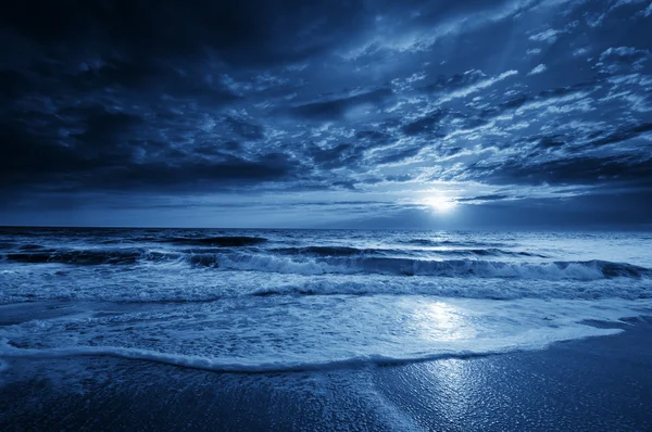 Полуночная голубая прибрежная луна с драматичным небом и катящимися волнами Стоковое Изображение