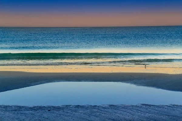 这张日出的照片是在墨西哥湾沿岸的佛罗里达清水海滩拍摄的 前景的阴影是由我住的旅馆投下的 一缕狭窄的阳光照亮了破浪和海滩 在遥远的清晨 — 图库照片