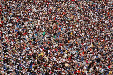 Large group of people attending a sporting event. The crowd is not identifiable as a Photoshop Dry Brush filter has been carefully applied. There is good detail but the brush stroke effect hides the individuals identity, making a great background for