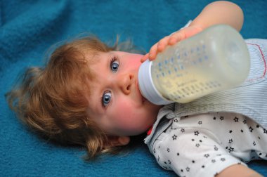 küçük kız mavi kanepe ve içecek süt şişesi üzerinde yalan