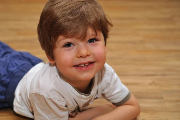 Felice bambino con i capelli castani sdraiato sul terreno di legno — Foto Stock